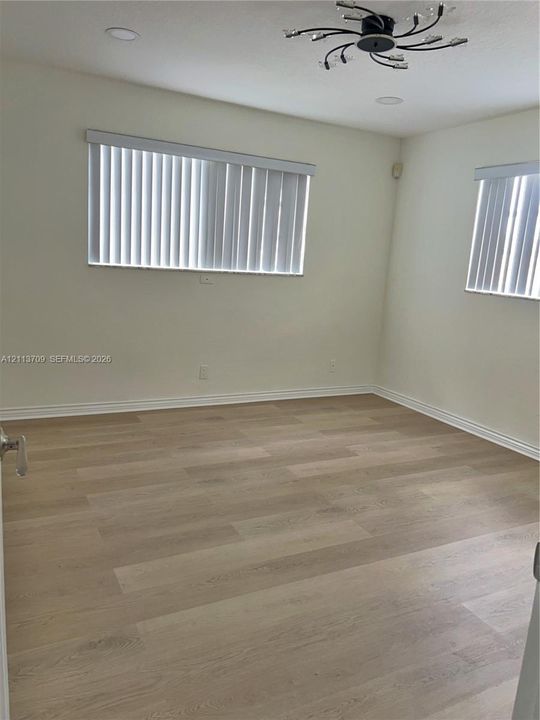 Light-filled room featuring wood-finish flooring, recessed lighting, a modern multi-arm ceiling fixture, and dual windows with vertical blinds