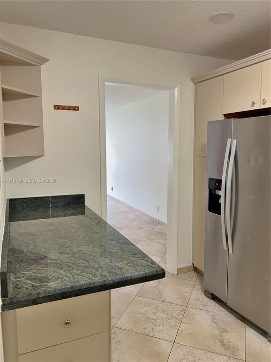 Kitchen featuring stone countertops, built-in cabinetry, an integrated refrigerator, open shelving, and tile flooring