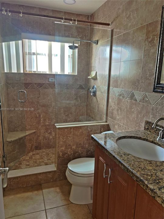 Bathroom featuring floor-to-ceiling stone-tiled walls, glass-enclosed walk-in shower with integrated corner bench, vanity with stone countertop, and undermount sink