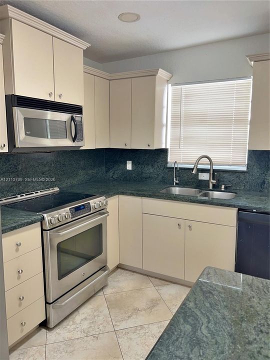 Kitchen featuring solid-surface countertops, custom shaker-style cabinetry, stainless steel appliances, a double-basin undermount sink with a gooseneck faucet, and tiled flooring