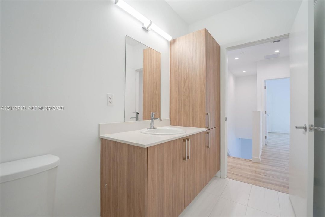 Bathroom vanity featuring wood-finish cabinetry, an integrated tall storage unit, a solid-surface countertop with an undermount sink, and a wall-mounted light fixture