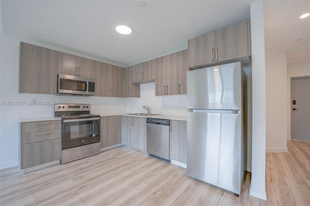 Kitchen featuring light-toned cabinetry, stainless steel appliances, wood-finish flooring, and solid-surface countertops