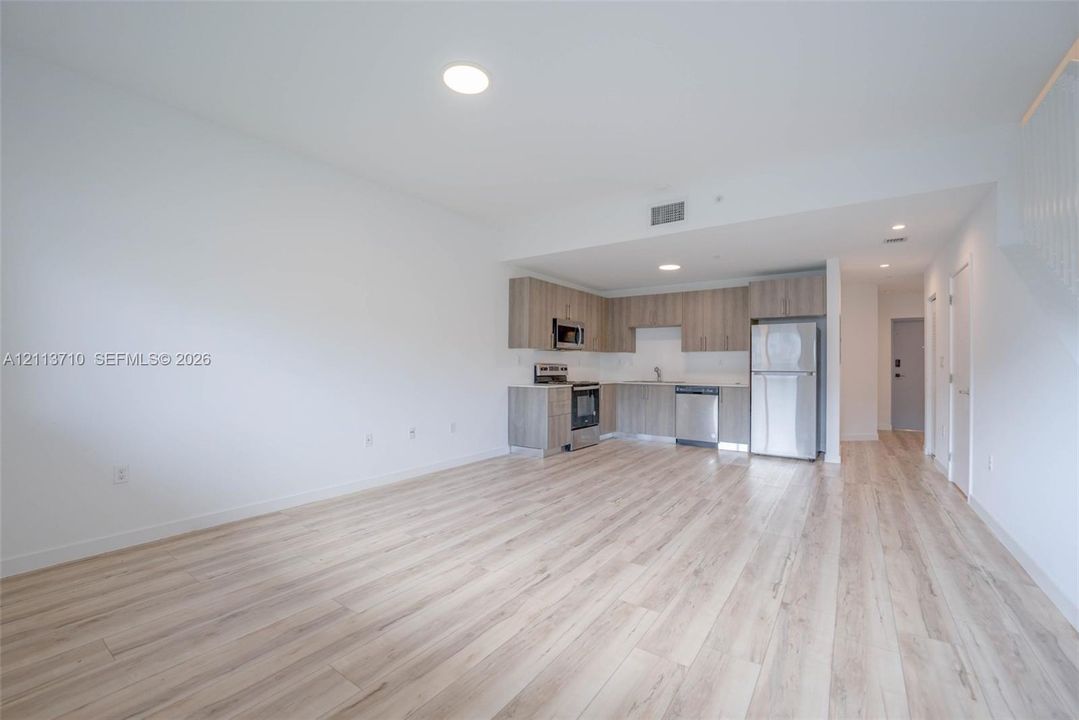 Open-concept interior featuring wood-finish flooring, cabinetry with a light-toned finish, stainless steel appliances, and recessed lighting