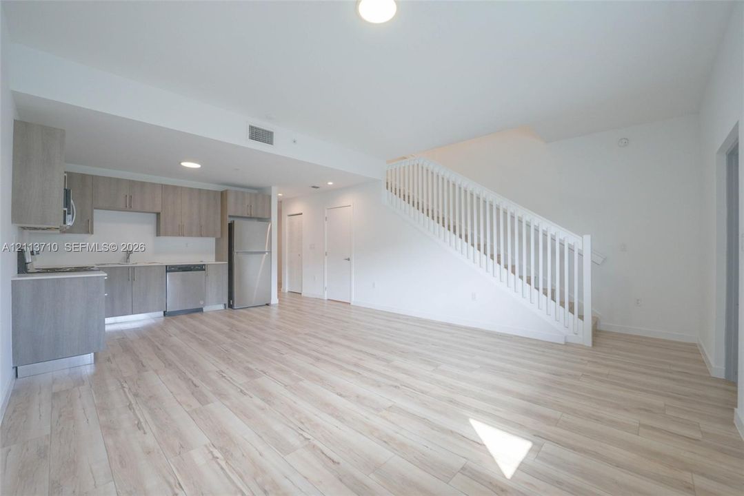 Kitchen featuring wood-finish cabinetry, stainless steel appliances, and wood-finish flooring, complemented by a staircase with white balusters