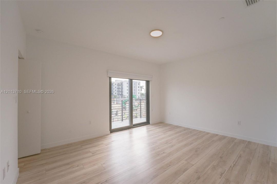 Interior space featuring wood-finish flooring, white walls, flush-mount ceiling lighting, and sliding glass doors with an integrated roller shade