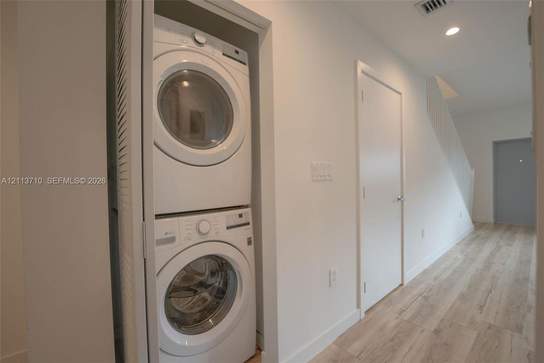 Stacked laundry unit within a dedicated closet, featuring wood-finish flooring and recessed lighting