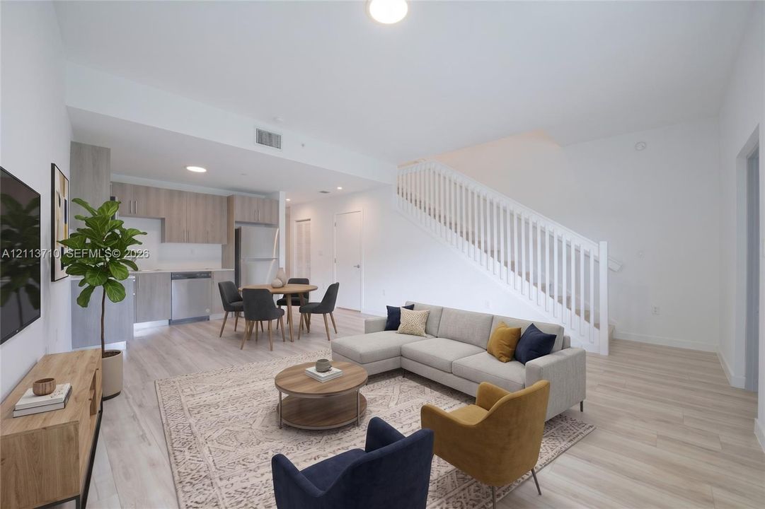 Open-concept interior featuring wood-finish flooring, white staircase railing, flat-panel cabinetry, and stainless steel kitchen appliances