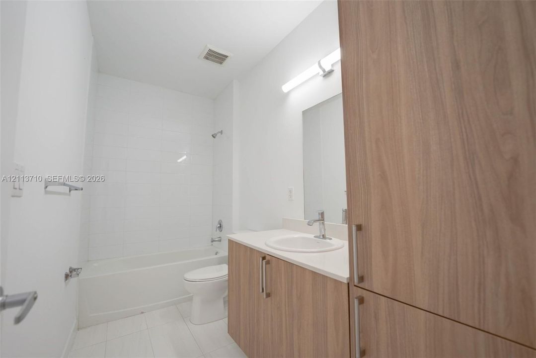 Bathroom featuring wood-finish cabinetry, a white countertop with an integrated basin, a soaking tub with wall-mounted plumbing fixtures, and tiled flooring