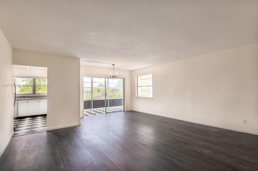 Open-concept interior featuring dark wood-finish flooring, neutral wall tones, multi-pane windows, and a classic chandelier