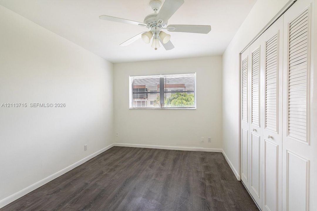 Wood-finish flooring, white louvered closet doors, and a ceiling fan with integrated lighting