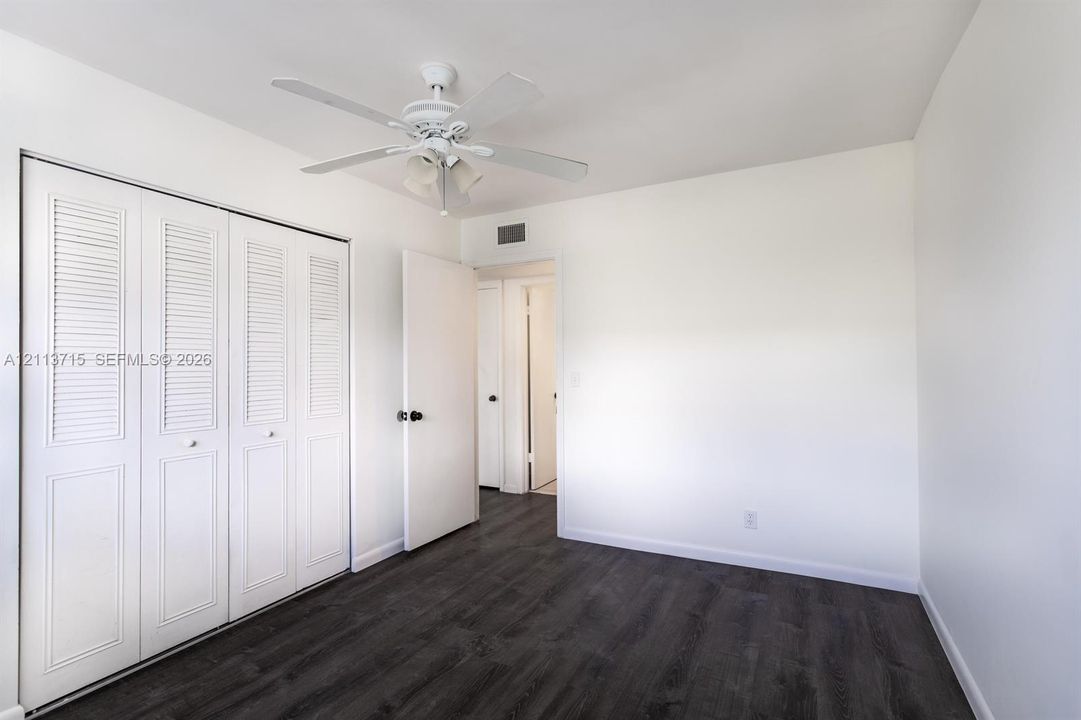 Room featuring wood-finish flooring, white walls, louvered bi-fold closet doors, and a ceiling fan with integrated lighting