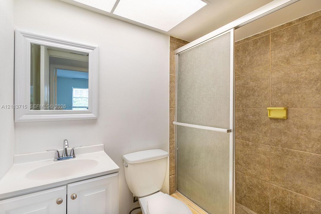 Bathroom featuring a vanity with a white countertop and oval basin, a wall-mounted framed mirror, a standard toilet, and a tiled shower enclosure with frosted glass sliding doors