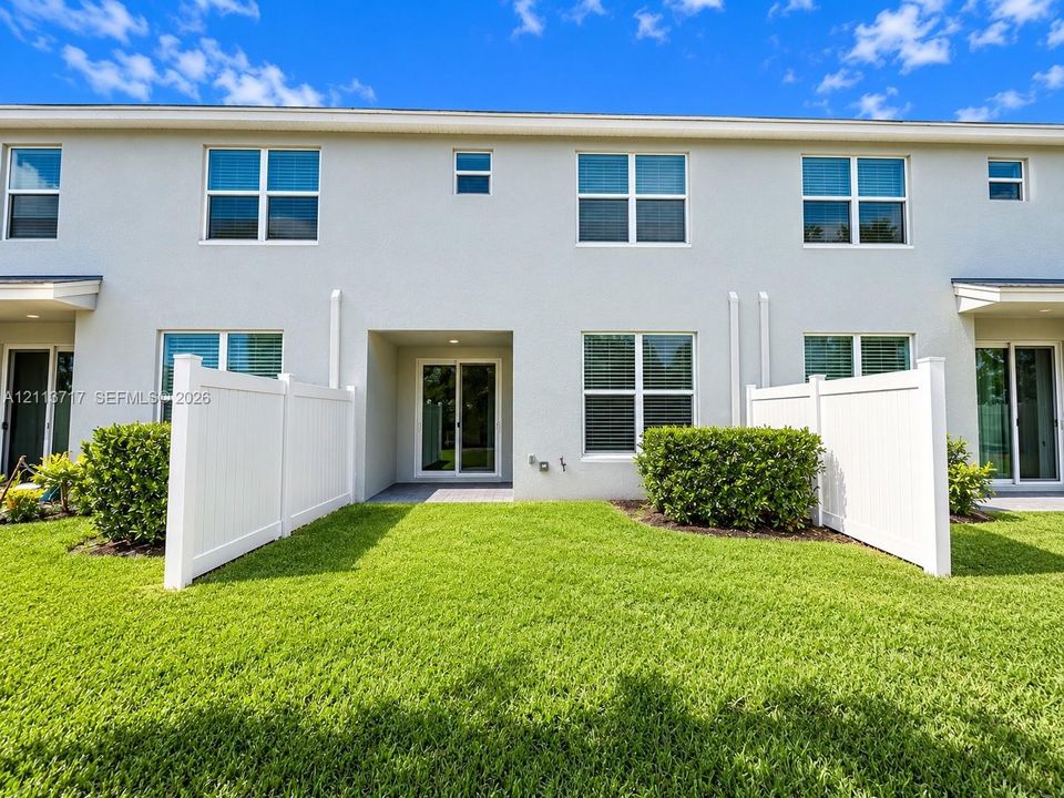 Stucco exterior featuring a paved rear patio, sliding glass doors, white vinyl privacy fencing, and manicured lawn