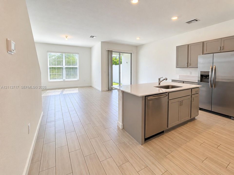 Kitchen featuring a central island with a solid-surface countertop, stainless steel appliances, neutral-toned cabinetry, wood-finish tile flooring, and recessed lighting