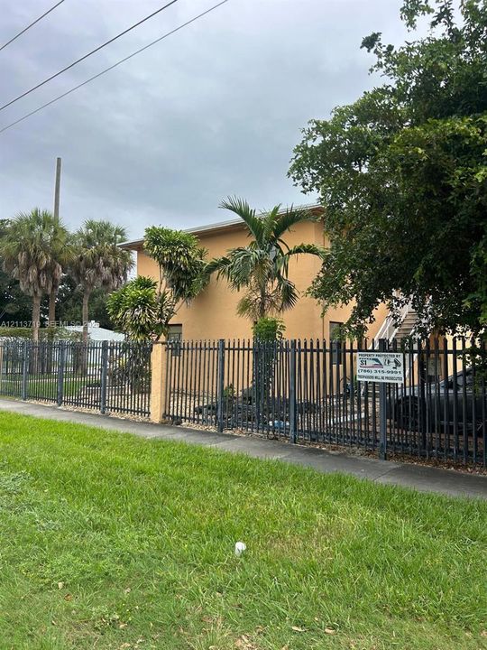 Two-story exterior featuring smooth stucco siding, metal picket perimeter fencing, and mature palm landscaping