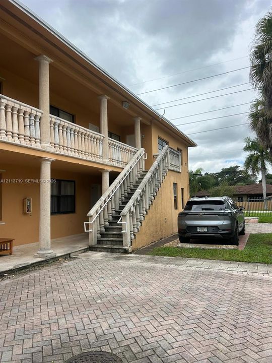 Stucco exterior featuring a two-story staircase, stone balustrade railings, support columns, and a brick paver driveway