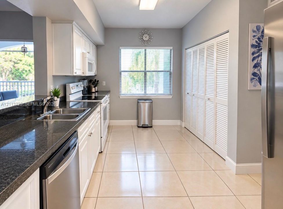 Kitchen featuring white shaker-style cabinetry, dark stone-finish countertops, stainless steel appliances, large-format tile flooring, and floor-to-ceiling louvered closet doors
