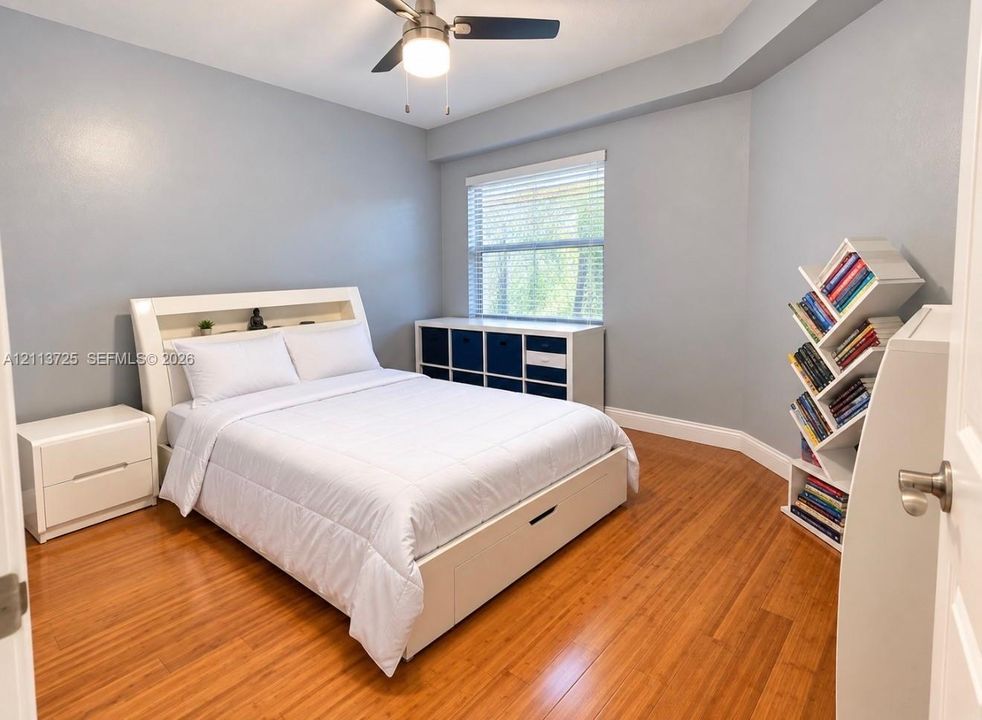 Room featuring wood-finish flooring, tray ceiling, and a ceiling fan with integrated lighting