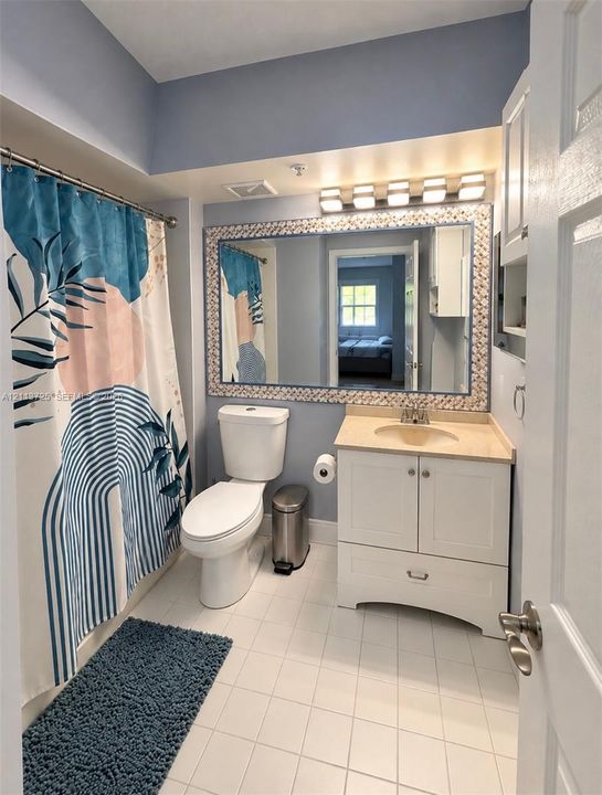 Bathroom featuring a white vanity cabinet with a stone-top integrated sink, a large framed wall mirror, a five-light vanity fixture, and tiled flooring