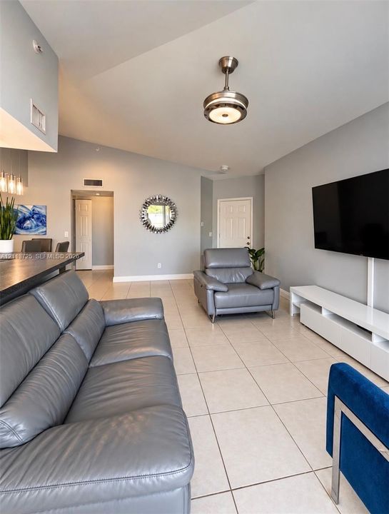 Living area featuring a vaulted ceiling, neutral tile flooring, and a modern drum-style flush-mount light fixture