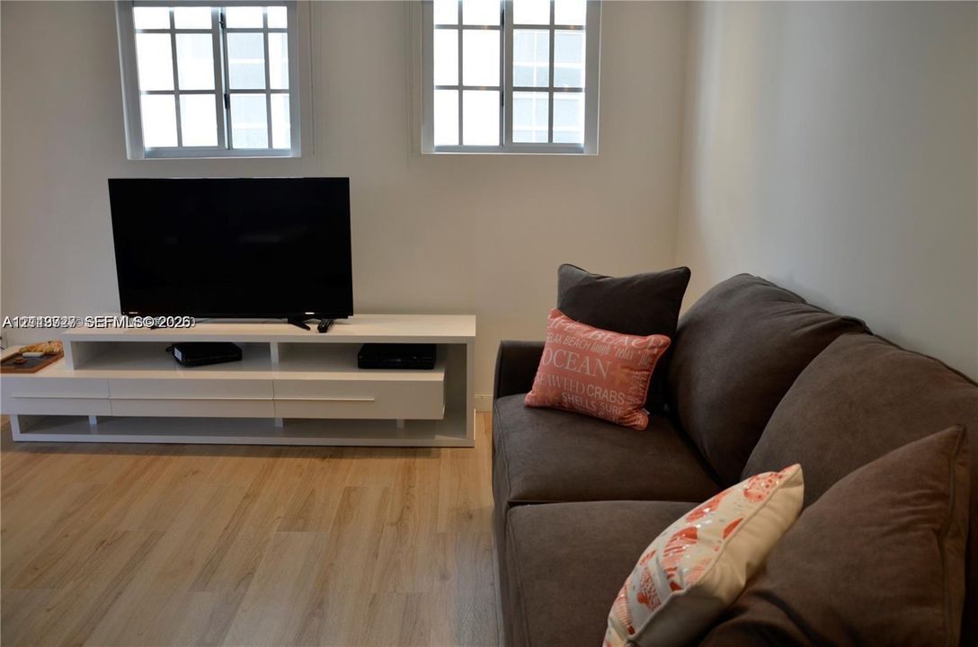 Light-toned wood-finish flooring, two dual-pane windows with grid detailing, and a white built-in media console