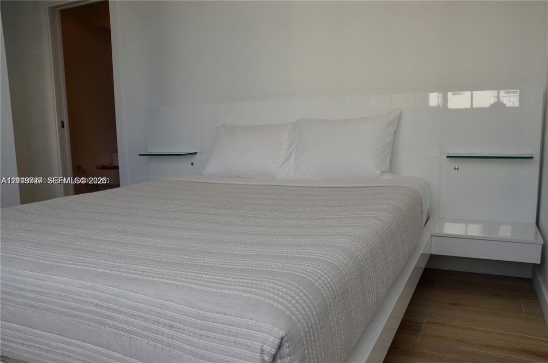 Built-in high-gloss white headboard featuring integrated glass shelving and floating side tables, complemented by wood-finish flooring