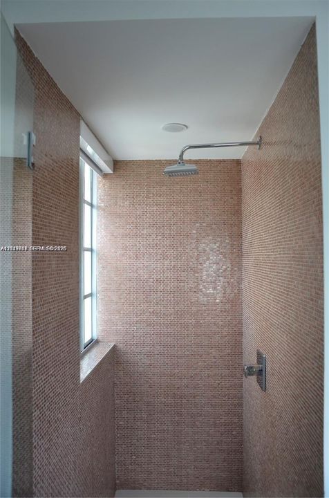 Shower stall featuring floor-to-ceiling mosaic tile, wall-mounted rainfall showerhead, single-handle pressure balance valve, and a window with a glass pane