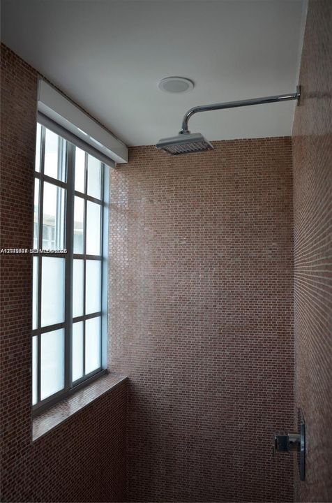 Shower enclosure featuring floor-to-ceiling mosaic tile, a grid-pane window with a stone sill, and a polished chrome rainfall shower head