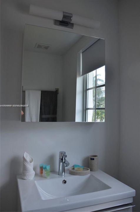 Wall-mounted rectangular mirror featuring a chrome-finished light fixture, integrated sink with a single-handle faucet, and built-in towel hardware