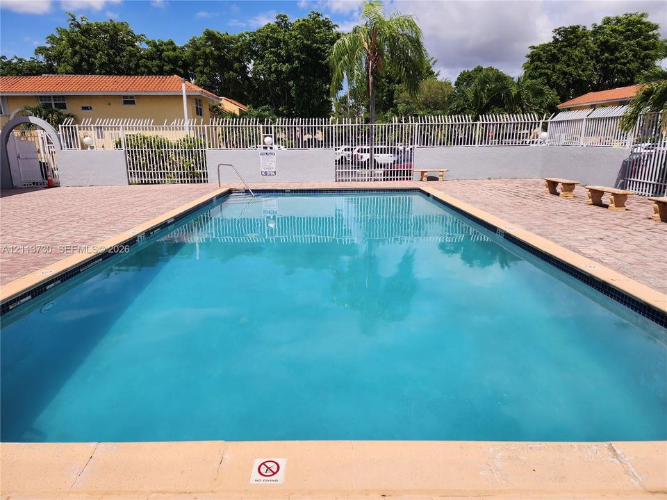 In-ground swimming pool featuring a concrete deck, metal perimeter fencing, and stone-finish bench seating