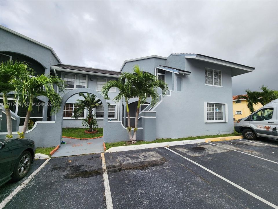 Stucco exterior featuring a paved walkway, a screened entry door, and a covered patio with tiled flooring