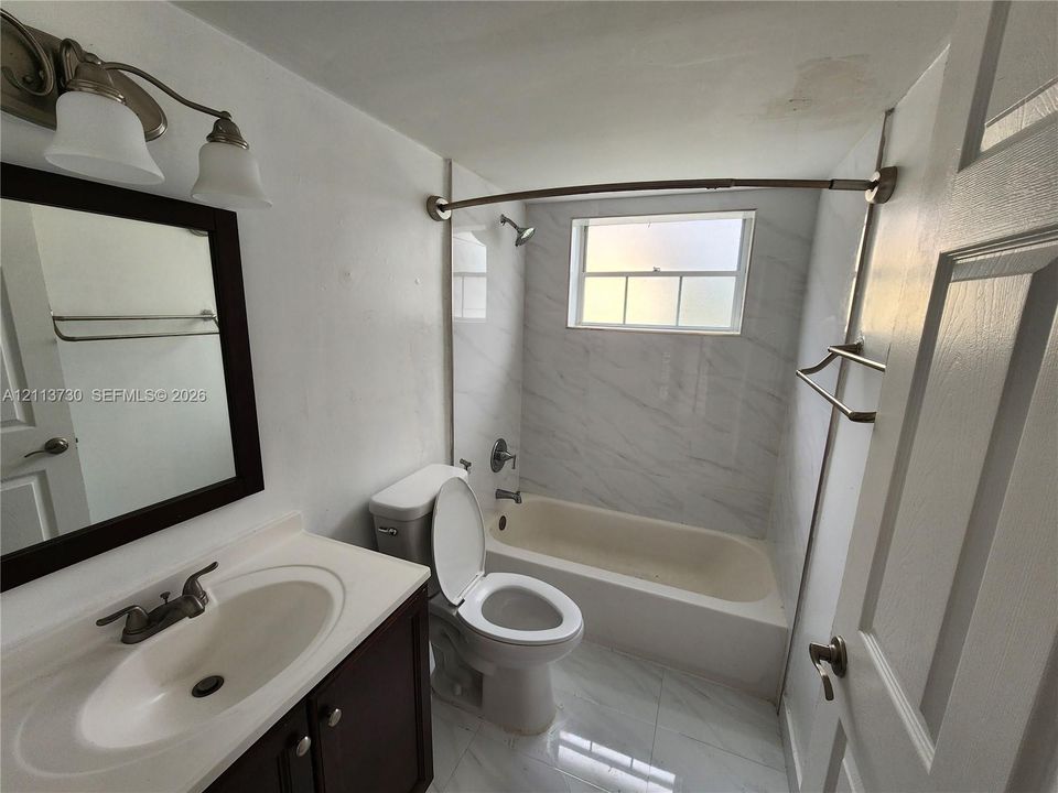 Full-height wall tile with marble-pattern finish, inset bathtub with chrome fixtures, and high-gloss floor tiling