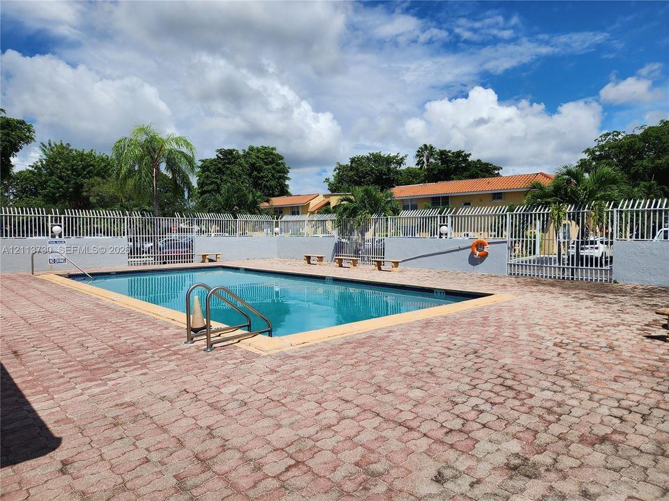 Outdoor swimming pool featuring a concrete paver deck, perimeter metal fencing, and integrated stainless steel ladder