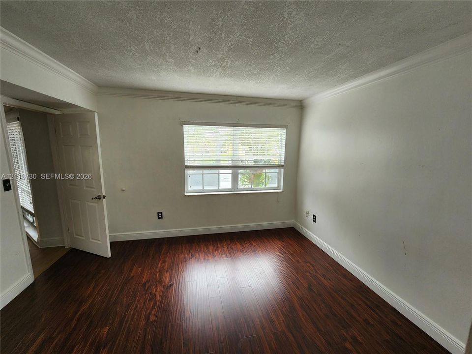 Interior space featuring wood-finish flooring, crisp white walls, crown molding, and a window equipped with horizontal blinds