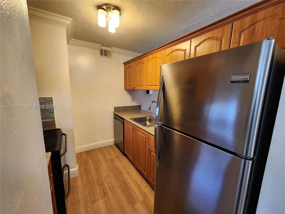 Kitchen featuring wood-finish cabinetry, stainless steel refrigerator, stone-composite countertops, stainless steel sink with gooseneck faucet, and wood-finish flooring