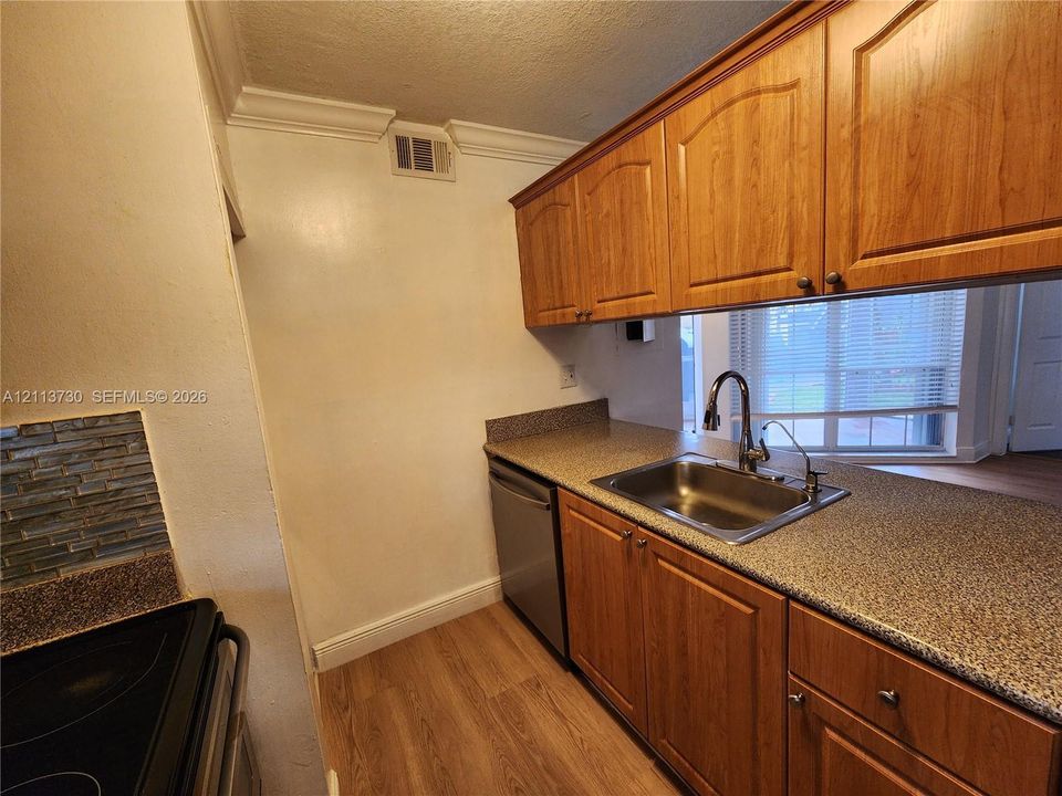 Kitchen featuring wood-finish cabinetry, stone-texture countertops, stainless steel sink with high-arc faucet, integrated dishwasher, and tile backsplash