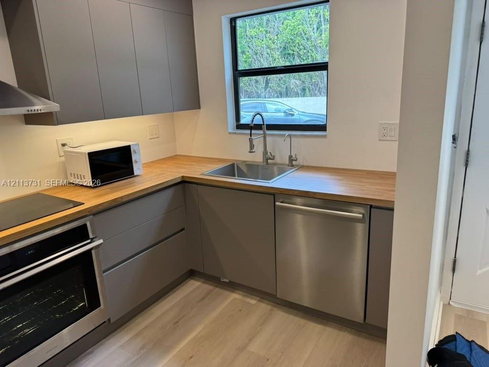 Kitchen featuring flat-panel gray cabinetry, wood-finish countertops, stainless steel appliances, and wood-finish flooring