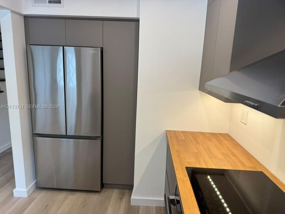 Kitchen featuring flat-panel cabinetry, stainless steel French door refrigerator, wood-finish countertop, glass cooktop, and stainless steel range hood