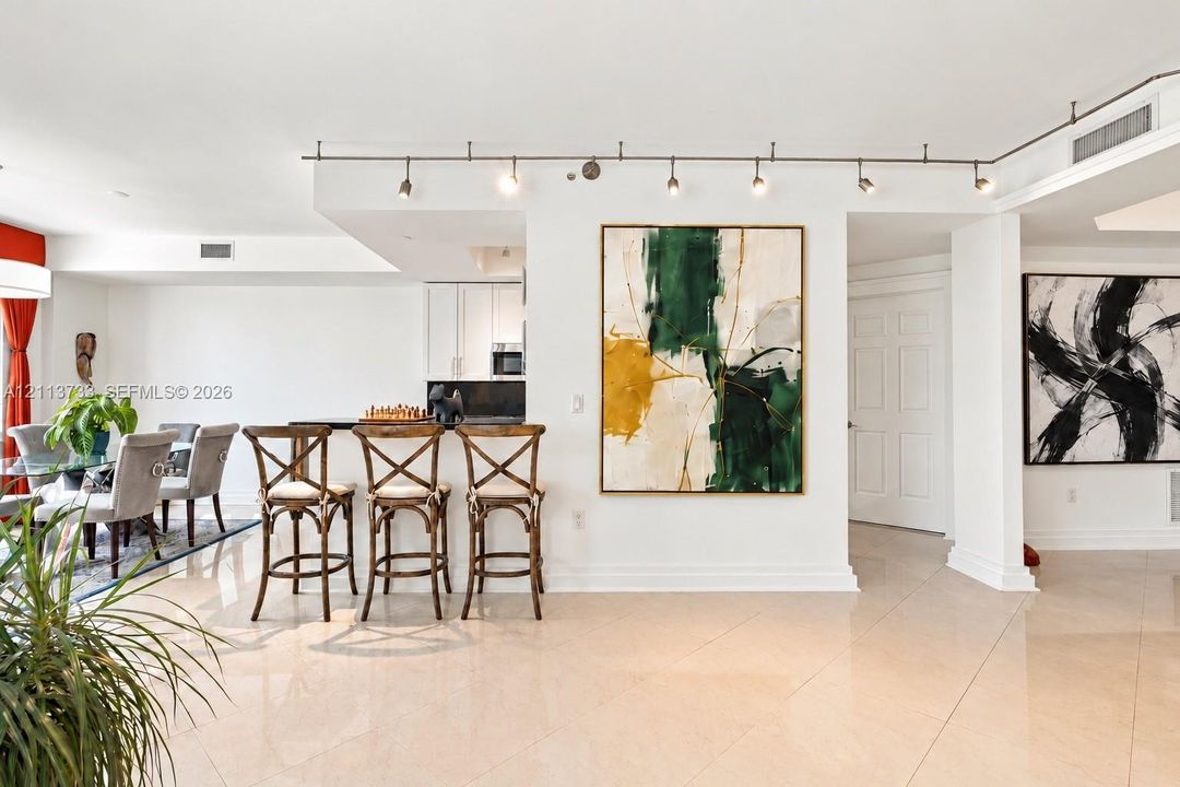 Open-concept interior featuring large-format tile flooring, recessed track lighting, and a kitchen breakfast bar