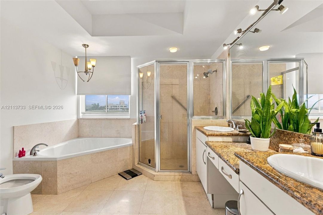 Bathroom featuring a corner soaking tub with stone surround, a glass-enclosed shower, dual-sink vanity with stone countertop, and recessed ceiling lighting