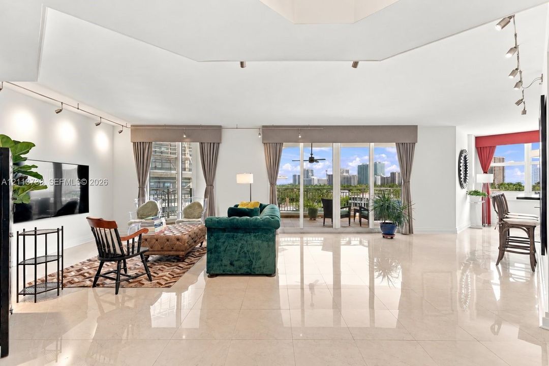 Spacious interior featuring high-gloss tile flooring, vaulted ceilings, adjustable track lighting, and multiple floor-to-ceiling glass panel doors providing access to a balcony