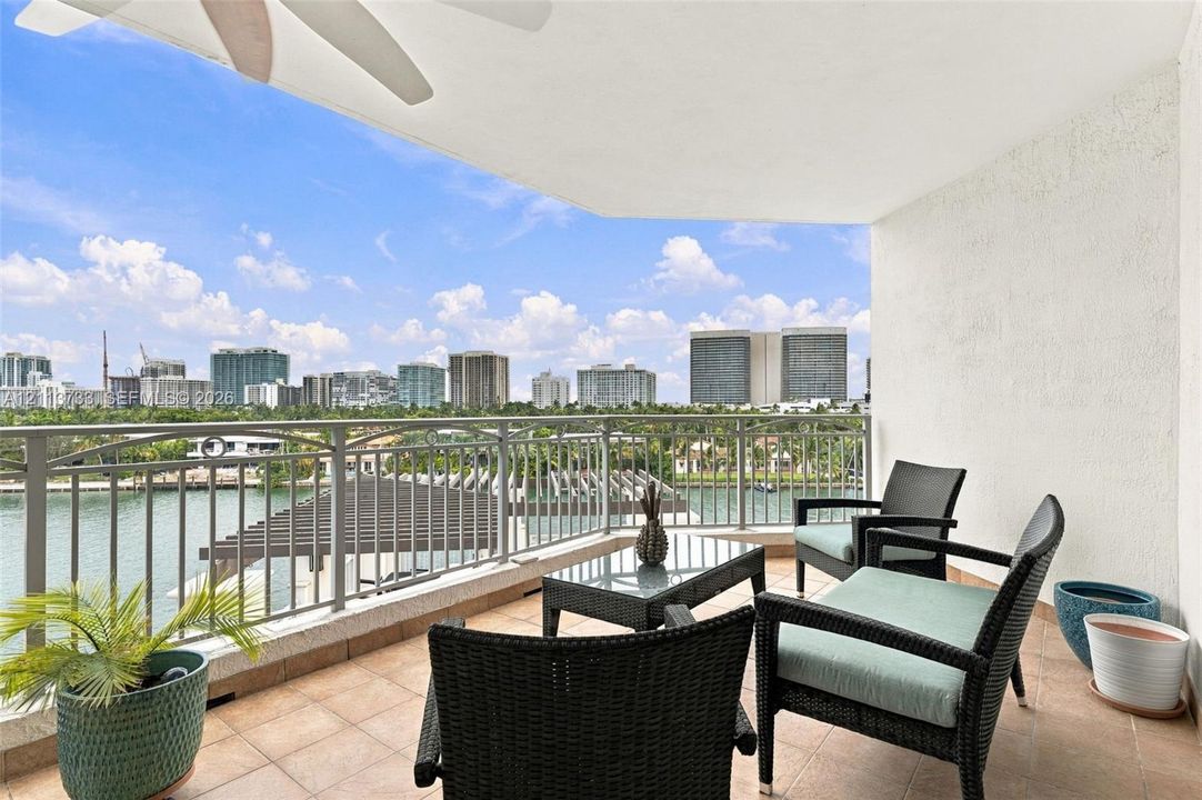 Covered balcony featuring tile flooring, a ceiling-mounted fan, and metal railings overlooking the water and urban skyline