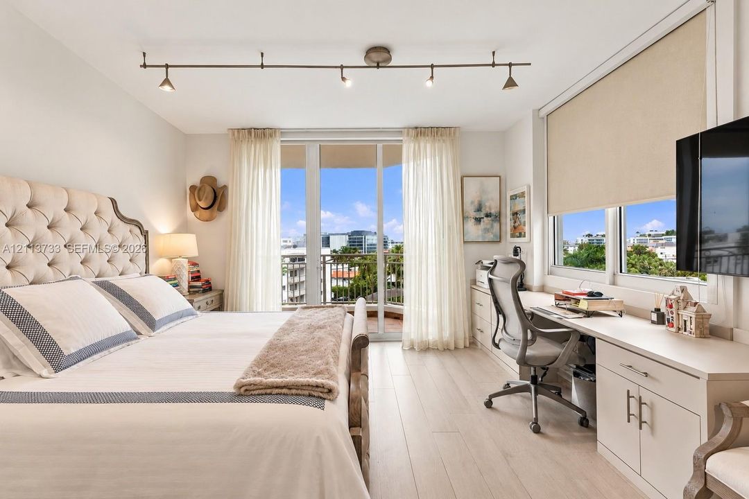 Wood-finish flooring, built-in cabinetry with desktop, floor-to-ceiling glass door opening to a balcony, and adjustable track lighting