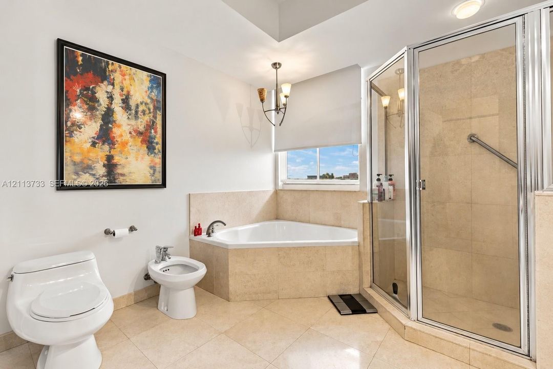 Corner soaking tub with stone tile surround, glass-enclosed shower, bidet, and tile flooring