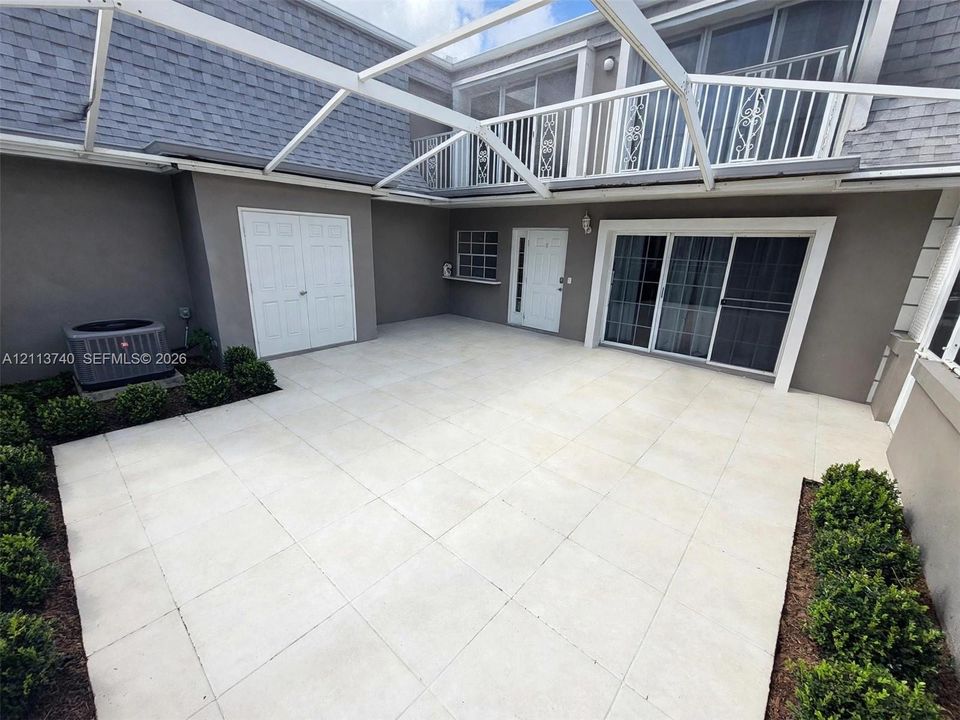 Screened-in patio featuring light-toned tile flooring, second-story balcony with metal railing, double-door storage access, and sliding glass entry doors