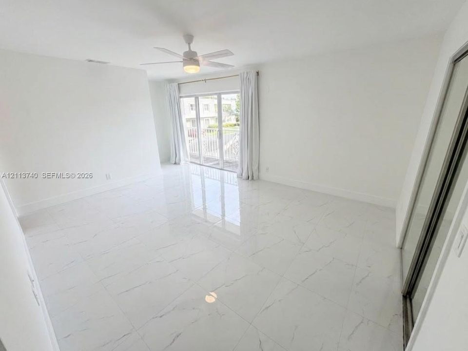 Large-format porcelain tile flooring with marble-style veining, ceiling fan with integrated lighting, and full-height sliding glass doors with direct exterior access