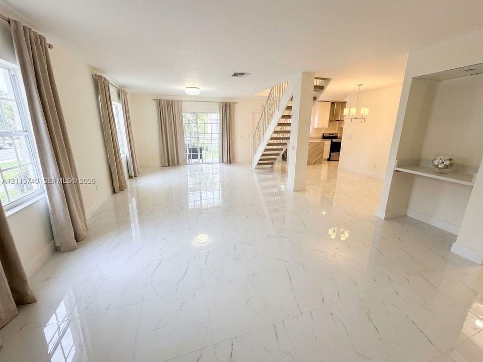 Open-concept interior featuring large-format porcelain tile flooring, sliding glass doors, a built-in recessed wall niche with a stone-surface counter, and a staircase with a metal railing