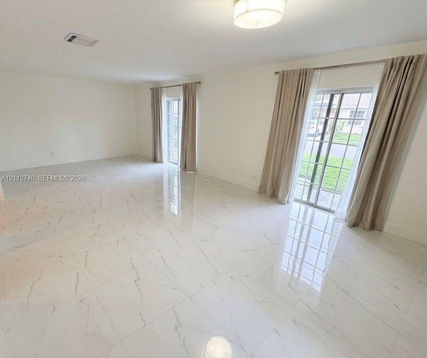 Polished large-format stone-finish tile flooring, dual sets of glass-paned sliding doors, and a flush-mount drum ceiling light fixture