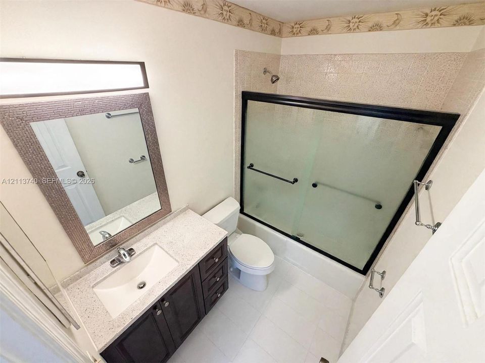 Bathroom featuring a dark wood vanity with stone-composite countertop, integrated sink, framed wall mirror, and a tub-shower combination with sliding glass doors