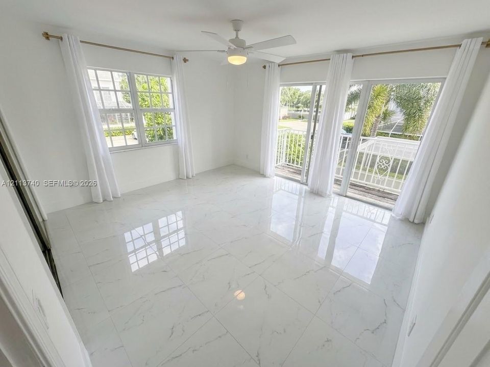 Large-format tile flooring, multi-pane windows, ceiling fan with integrated lighting, and sliding glass doors with access to a railed balcony